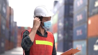 İşçi işçi maskesini ve kaskını çıkarıp açık hava depo fabrikasında yeşil yansıtıcı güvenlik elbisesi giyiyor. Güvenlik sektörü çalışanı kavramı.