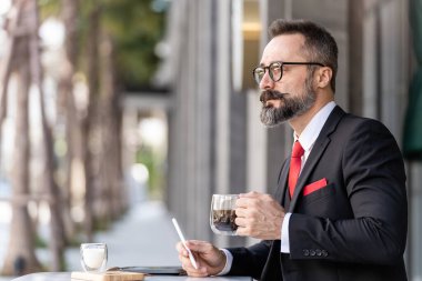 Zeki takım elbiseli son sınıf öğrencisi açık hava kahve masasında oturup düşünüyor..