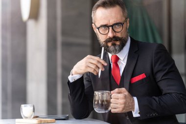 Zeki takım elbiseli son sınıf öğrencisi açık hava kahve masasında oturup düşünüyor..