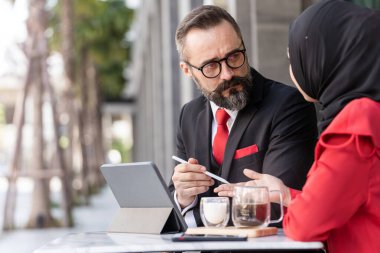 Zeki takım elbiseli son sınıf öğrencisi açık hava kahve masasında İslamcı kadınla konuşuyor. Teknoloji laptop aygıtı ile iş sunumunu kavra.