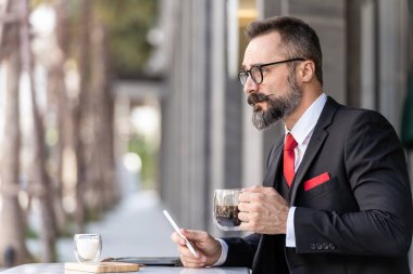 Zeki takım elbiseli son sınıf öğrencisi açık hava kahve masasında oturup düşünüyor..