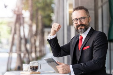Zeki takım elbiseli ve kendine güvenen son sınıf öğrencisi açık kahve masasında oturuyor..