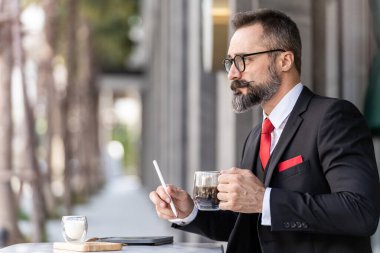 Zeki takım elbiseli son sınıf öğrencisi açık hava kahve masasında oturup düşünüyor..