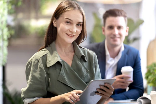 Portrait of happy woman holding tablet device and sitting at coffee cafe counter bar with people colleague at background. Concept business coffee time with smart technology working.