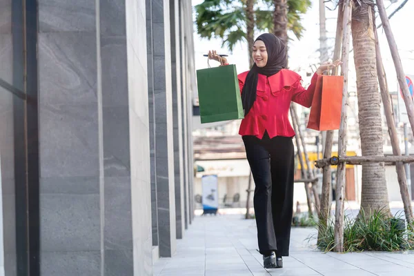 喜气洋洋的穆斯林女人 身穿红色衣服 提着购物袋 走在户外街道上 购物旺季 圣诞节及新年的概念活动 — 图库照片