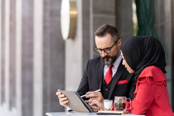 senior man in smart business suit talking to islam woman at outdoor coffee table. Concept business presentation with technology laptop device.