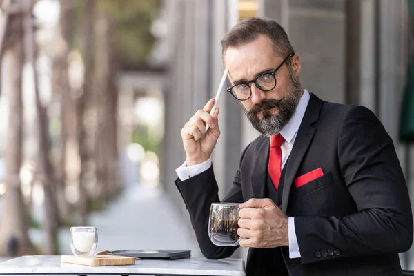 senior man in smart business suit thinking and sitting in outdoor coffee table.