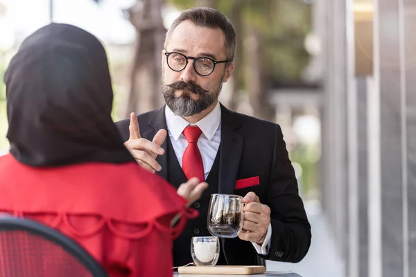 senior man in smart business suit talking to people and sitting in outdoor coffee table.
