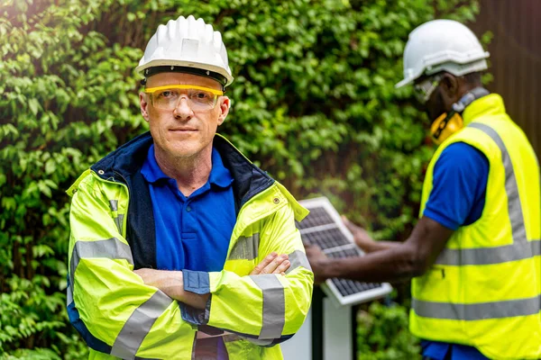 工場労働者技術者の男は 持続可能な技術のための太陽電池パネルをチェックフロントワーカーで緑の作業スイートのドレスと安全ヘルメットに自信を持って立って — ストック写真