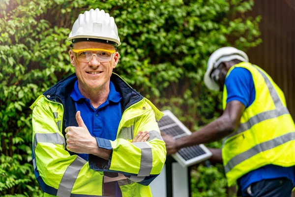 工場労働者技術者の男は 持続可能な技術のための太陽電池パネルをチェックフロントワーカーで緑の作業スイートのドレスと安全ヘルメットに自信を立って — ストック写真