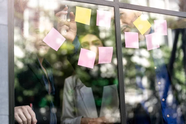 business people brainstorming putting sticky notes on glass window wall in office. Window glass reflection daylight and environment nature. Creative group startup business meeting for new idea.