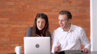 Erkek ve kadın iş arkadaşı ofis işyerinde defter ve tabletle konuşuyor ve görüşüyorlar. Birlikte çalışma alanındaki kırmızı tuğlanın arkaplanı.