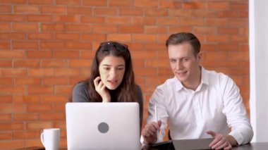 İş arkadaşım dizüstü bilgisayar kullanıyor, projeyi tartışıyor ve kahve içiyor. Kadın ve erkek partnerler bilgisayar ekranına bakıp konuşuyorlar. Çalışma alanındaki kırmızı tuğlanın arkaplanı.