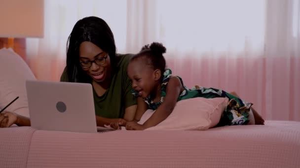 幸せな家族アフリカの母親と子供はコンピュータのラップトップで一緒に勉強しながら 寝室に横になります 学校に子供を準備する概念 — ストック動画