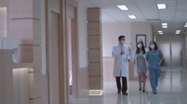 Hastanede, koridorda dikilirken maske takan Meşgul Doktorlar konuşuyor. Arka plandaki hasta ve personel koğuşta yürüyor. konsept tıp insanları Modern Temiz Tıp Tesisinde yaşam.