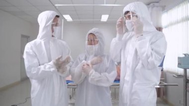 Doktorlar ve hemşireler ayakta durup koruyucu giysiyi kontrol ediyorlar. Hemşireler hastanedeki temiz odada maske takan hastaları muayene ediyorlar. İnsanlarda Covid-19 ya da koronavirüs hastalığı vardı..