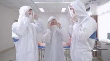 Doktorlar ve hemşireler ayakta durup koruyucu giysiyi kontrol ediyorlar. Hemşireler hastanedeki temiz odada maske takan hastaları muayene ediyorlar. İnsanlarda Covid-19 ya da koronavirüs hastalığı vardı..