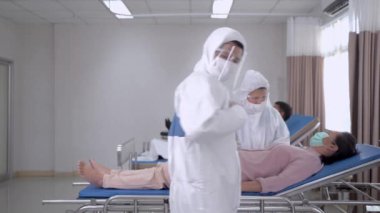Tıbbi doktor kişisel koruyucu giysi giyiyor ve kendine güveniyor. Hemşireler hastanenin temiz odasında hastaları muayene ediyor. İnsanlarda Covid-19 ya da koronavirüs hastalığı vardı..