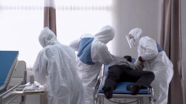 Doktorlar ve hemşire, hastane yatağında ani bir hastalık ve nöbet geçiren hastayı muayene ediyor. Adamın Covid-19 ve Coronavirus hastalığı varmış..
