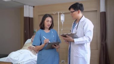 Doktor ve hemşire hasta Asyalı yaşlı bir adamın yatakta dinlenirken gösterdiği semptom ve tedaviyi araştırmak için konuşuyor. Modern hastane odasındaki VIP sınıfında tıbbi tedavi kavramı.