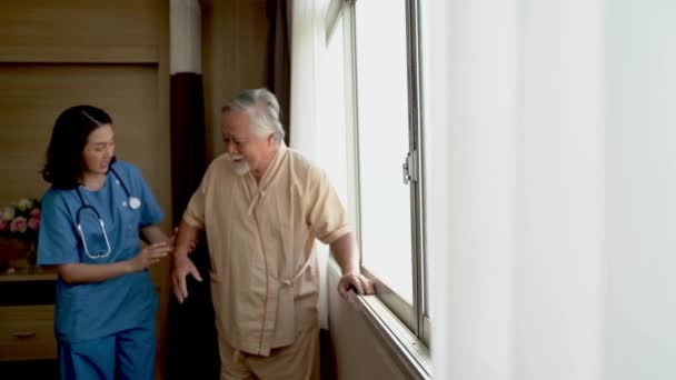 窓の近くを歩いているアジア系の高齢者の病気の高齢者はリラックスしており 医師は彼を世話する 現代の病院の部屋でVipクラスでコンセプト医療 — ストック動画