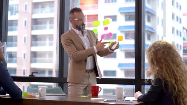 사업가인 시니어는 프로젝트를 제공하고 아이디어를 종이에 회의실에서 스카이라인 타워의 벽으로 — 비디오