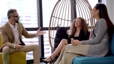 Çok ırklı iş adamları lobide toplanıp eğleniyorlar. İçerde toplantı yapan rahat genç yöneticiler konsepti. Ofis lobisinde oturup iş konuşan çok ırklı bir grup insan..