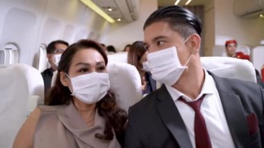 Yüzü maskeli iş adamı ve kadın uçak koltuğunda oturup konuşuyor. Sağlık koruması için hava taşımacılığında yeni bir normal kavram.