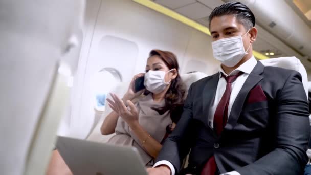 戴面具的商人 他使用笔记本电脑 坐在飞机座位上 女人使用智能手机 坐在新的窗口 保护健康的航空交通新概念 — 图库视频影像
