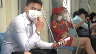 Yüzü maskeli bir adam akıllı telefon kullanıyor ve metroda toplu taşıma araçlarıyla seyahat eden insanlarla birlikte oturuyor. Salgın Hastalıklı Corona Virüsü ile yeni bir normal yaşam.