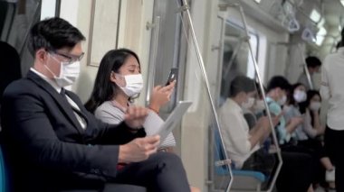 İş adamı akıllı tablet kullanıyor ve metro metrosunda akıllı telefon kullanarak yüz maskeli bir kadının yanına uzaklaşıyor. Salgın Grip Corona Virüsü ile yeni bir yaşam kavramı.