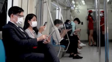 İş adamı akıllı tablet kullanıyor ve metro metrosunda akıllı telefon kullanarak yüz maskeli bir kadının yanına uzaklaşıyor. Salgın Grip Corona Virüsü ile yeni bir yaşam kavramı.