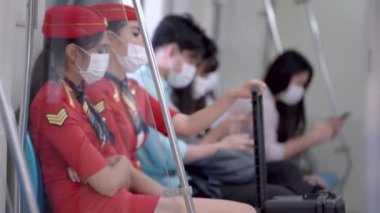 Üniformalı kabin görevlisi kadın yüz maskeli ve metro metrosunda toplu taşıma araçlarıyla seyahat eden insanlarla birlikte oturuyor. Salgın Hastalıklı Corona Virüsü ile yeni bir normal yaşam.