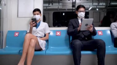 Yüz maskeli insanlar akıllı telefon kullanır ve metro istasyonunda otururlar. Kadınlar iş kadınlarının salgın hastalıkları önlemek için yaklaşmasını yasakladı. Salgın hastalıklar için sosyal uzaklık salgını 19 Corona Virüsü.