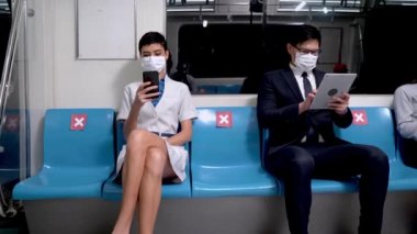 Yüz maskeli insanlar akıllı telefon kullanır ve metro istasyonunda otururlar. Kadınlar iş kadınlarının salgın hastalıkları önlemek için yaklaşmasını yasakladı. Salgın hastalıklar için sosyal uzaklık salgını 19 Corona Virüsü.