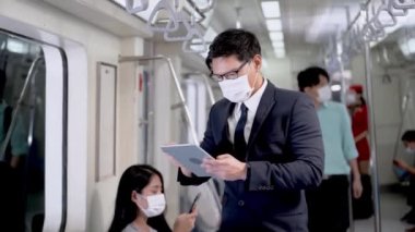Yüz maskeli iş adamı akıllı tablet cihazlar kullanıyor ve metro metrosunda toplu taşıma araçlarıyla seyahat eden insanlarla birlikte duruyor. Salgın Hastalıklı Corona Virüsü ile yeni bir normal yaşam.