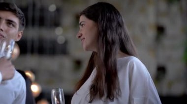 Ortak başarılarını kutluyorlar. Kadın ve erkek neşeli iş adamları şampanya içip sohbet ederken diğer insanlar arka planda iletişim kuruyor..