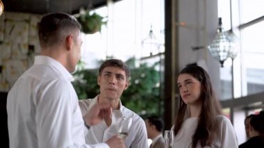 Ortak başarılarını kutluyorlar. Üç neşeli iş adamı şampanya içip sohbet ederken diğer insanlar arka planda iletişim kuruyor..