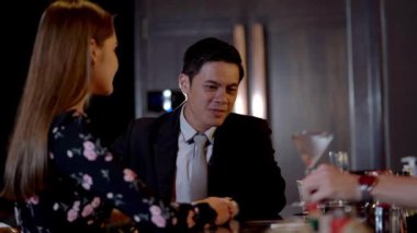 İnsanlar gece kulübünde kutlamak için tezgahta oturup kokteyl içiyorlar. Genç adam, gülümseyen barmen profesyonel olarak şişeyi kullanarak içkiyi karıştırır..