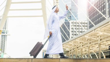 Arap bir adam iş şehrinde bavul taşır modern çelik yapısı ve dış duvarı modern binası olan iş simgesi bir şehirde yürür. 