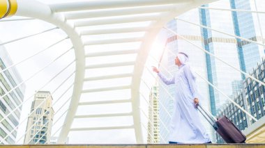 Arap bir adam iş şehrinde bavul taşır modern çelik yapısı ve dış duvarı modern binası olan iş simgesi bir şehirde yürür. 