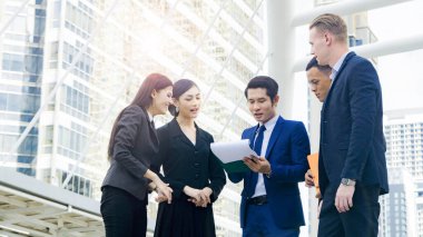 Çok uluslu iş adamları. Zeki erkek ve kadınlar konuşur ve projeyi sunarlar. Evrak işleri ile birlikte şehir meydanındaki modern bina boyunca yaya yürüyüşünde iyi hissedersiniz.