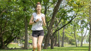 Asyalı, yakışıklı, sağlıklı, sıska, genç bayan ağırlık antrenmanından önce ısınıyor ya da açık hava bahçesinde koşuyor.