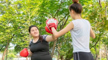 Şişman kadın formda ve formda bir kız ile diyet yapıyor. Spor yapıyor, ısınıyor ve açık hava parkında boks yapıyor..
