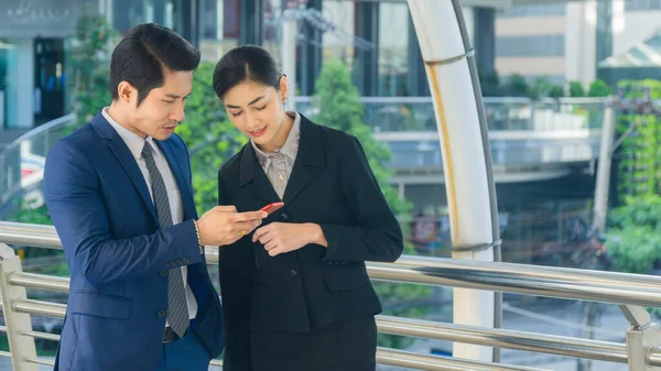 Excited business man and woman receiving good news on line in a smart phone outside on outdoor