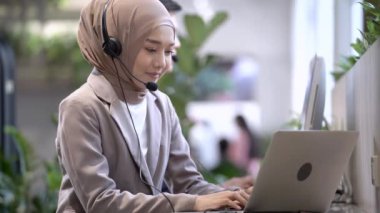 Çağrı merkezi operatörü kadın mikrofon kulaklığıyla çalışıyor ve bar tezgahında dizüstü bilgisayar kullanıyor. Doğadaki biyofili iç mekanda dekorasyon fabrikası var..