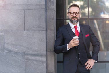 Takım elbiseli bir adam elinde kahve tutuyor. Sabahın köründe kahve saatinde iş hayatı. Taze ve mutlu hisseden adam, başarısından emin..