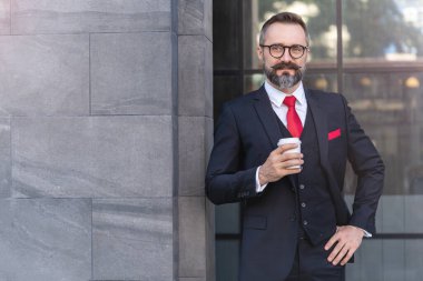 Takım elbiseli bir adam elinde kahve tutuyor. Sabahın köründe kahve saatinde iş hayatı. Taze ve mutlu hisseden adam, başarısından emin..