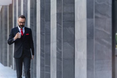 Takım elbiseli üst düzey yönetici elinde bir fincan kahve ve dizüstü bilgisayar tutuyor. Sabahın köründe kahve saatinde iş hayatı. Taze ve mutlu hisseden adam, başarısından emin..