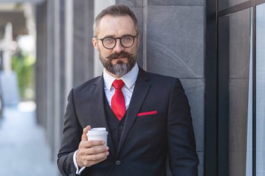 Takım elbiseli üst düzey yönetici elinde bir fincan kahve ve dizüstü bilgisayar tutuyor. Sabahın köründe kahve saatinde iş hayatı. Taze ve mutlu hisseden adam, başarısından emin..